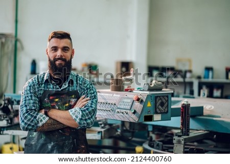 Male worker posing while using printing machine in a workshop