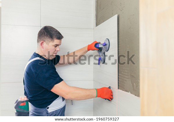 Male worker professional master laying ceramic\
tiles on the wall in the bathroom. Portrait experienced repairman\
man placing large size tiles. builder installing tile at repair\
renovation work\
