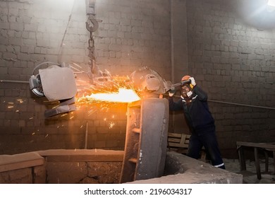 A male worker in a protective helmet, respirator, overalls manages heavy grinding equipment for cast iron concrete tubing with flying sparks in the workshop of an industrial plant.