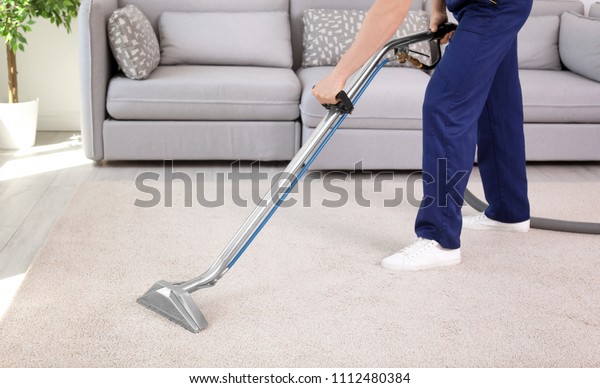 Male worker removing dirt from carpet with\
professional vacuum cleaner\
indoors