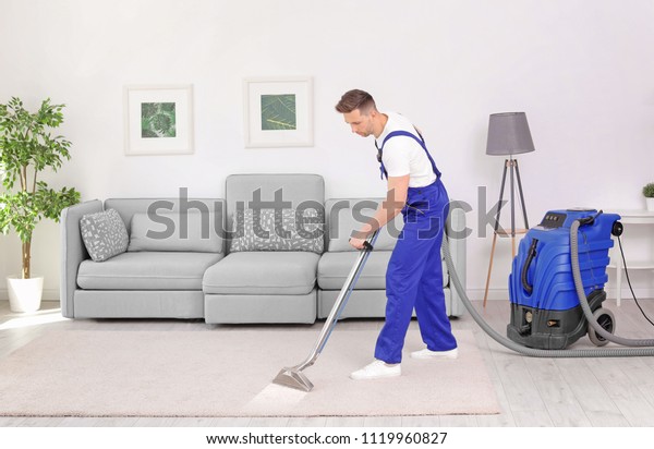 Male worker removing dirt from carpet with\
professional vacuum cleaner\
indoors