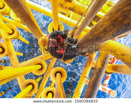 Male worker rope access  inspection of thickness offshore drill yellow oil and gas production petroleum pipeline.