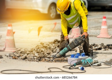 Male worker with safety equipments drilling concrete repairing driveway surface with jackhammer,danger sign concept.
 Professional worker.