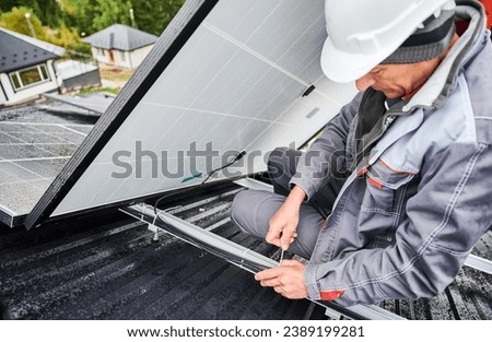 Male worker securing cables by special tie. Solar battery installation on roof of house. Man engineer in white helmet securing all cables of solar PV panel together.
