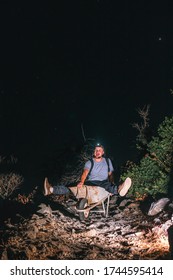 A Male Worker Is Sitting In A Wheelbarrow. Night View. Headlamp Illuminates The Trail. The Concept Of Heavy Utility And Construction Work In The Mountains On A Night Shift. Vertical Photo. Fun