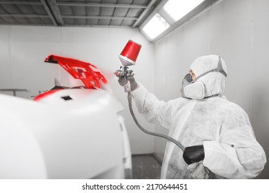 Male Worker Sprays Red Paint With Spray Gun On Car Bumper Part In Car Maintenance Service Paint Room.