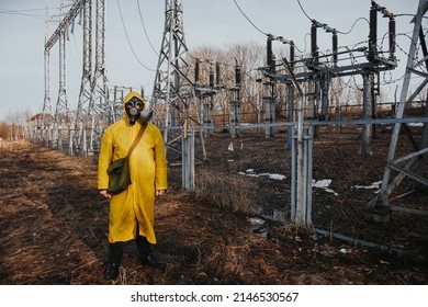 male worker standing on territory of power station with high voltage electricity tower on background. Environmentalist wearing protective uniform, gas mask.