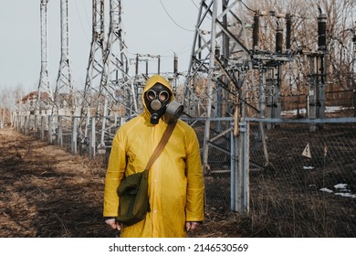 male worker standing on territory of power station with high voltage electricity tower on background. Environmentalist wearing protective uniform, gas mask.