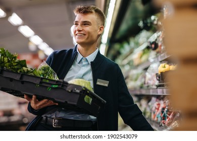 Male Worker Stocking Up The Vegetable Section In Supermarket. Man Working In A Vegetable Section Of A Grocery Store.