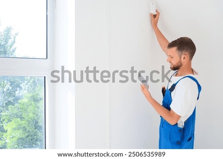 Male worker with tablet computer installing alarm system in room