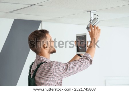Male worker with tablet computer installing alarm system in room