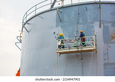 The male worker takes the cable car holding an industrial painting brush used for shell plate tank oil surface painted gray color coating.