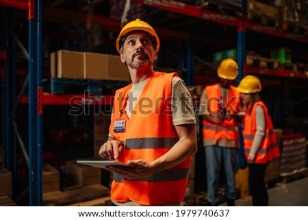 Male worker using digital tablet and oversees shelves in warehouse