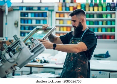 Male worker using screen printing film and a printing machine in a workshop - Shutterstock ID 2085526753