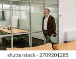 Male worker walking and smiling while looking ahead and holding hand in pocket, in hall, during retirement