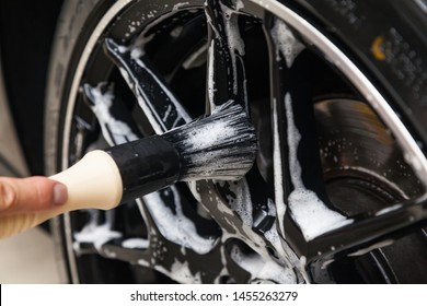 A Male Worker Washes A Black Car With A Special Brush For Cast Wheels And Scrubs The Surface To Shine In A Vehicle Detailing Workshop. Auto Service Industry.