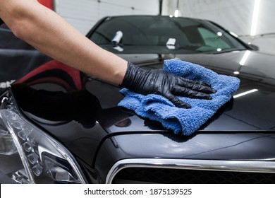 A male worker washes a black car, wiping water with a soft cloth and microfiber, cleaning the surface to shine in a vehicle detailing workshop. Auto service industry. - Powered by Shutterstock