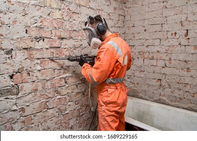Male Worker Wearing Full Face Respirator Mask And Ear Defenders For Working In Dusty And Noisy Environment While Using Hammer Drill.