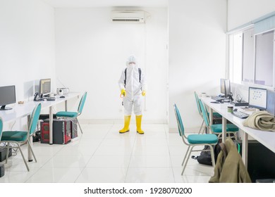 Male Worker Wearing Hazmat Suit While Cleaning Office Interior With Disinfectant Spray During Coronavirus Pandemic