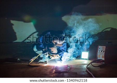 Male  worker wearing protective clothing repair  bottom plate storage tank industrial construction smoke spotlight inside confined spaces.