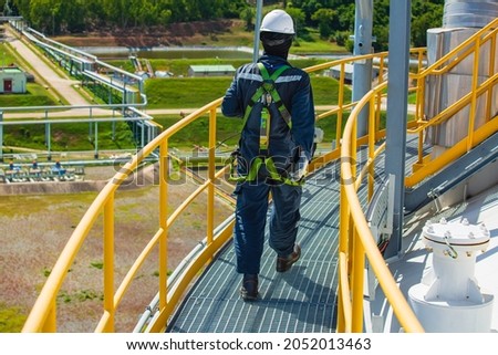 Male worker wearing safety first harness and safety lone working at high handrail place on open top tank roof oil