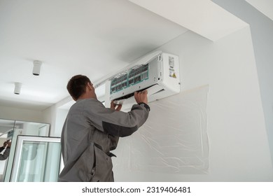 Trabajador masculino con uniforme que instala aire acondicionado en el apartamento durante la temporada de verano, técnico de mantenimiento en el interior reparando el sistema HVAC, revisando y reemplazando el filtro de CA