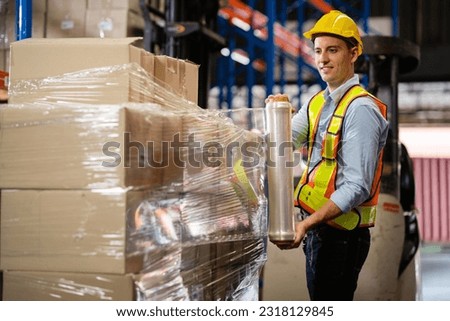Male worker wrapping parcel in stretch film on cargo in large factory warehouse Logistics and export concept.