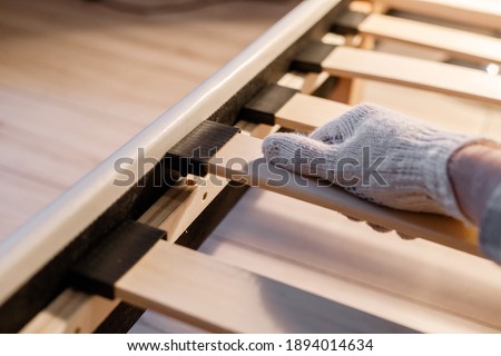 Male worker's hand in glove assembling bed, connecting slats to bed frame
