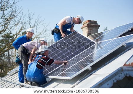 Male workers installing solar photovoltaic panel system. Group of electricians mounting blue solar module on roof of modern house. Alternative energy ecological concept.