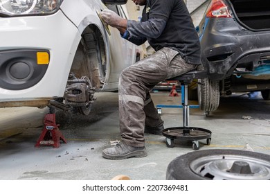 male working on car while sitting on creeper chair body repair panel beating sanding car 