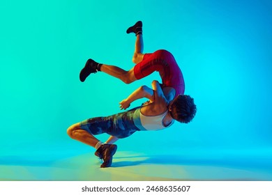Male wrestlers engage in physical battle, each striving for victory, competing, training against blue background in neon. Concept of combat sport, martial arts, competition, tournament, athleticism