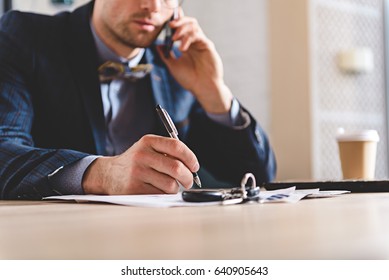 male writing at table while talking on phone