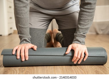 Male Yoga Practitioner In Grey Clothes Rolls Out His Yoga Mat