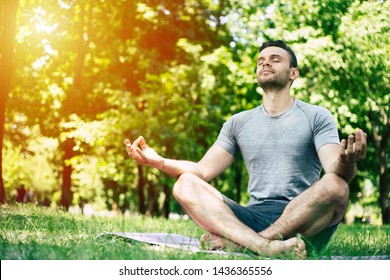 Male Yoga Relaxation. Sporty And Slim Handsome Young Man Is Doing Yoga Exercises In City Park Outdoors. Healthy Lifestyle And Strong Soul And Body