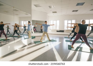 Male Yoga Teacher Giving Class To Female Group In Sunny  Yoga Studio With Bug Mirror 