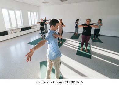 Male Yoga Teacher Giving Lesson To Female Group In Sunny Yoga Studio