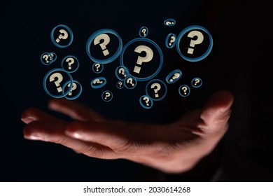 A male's hand holding illustrated question marks in blue circles on a black background