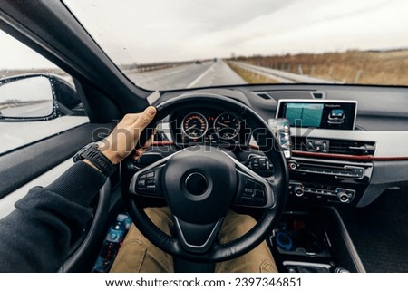A male's hand on steering wheel driving a car on highway.