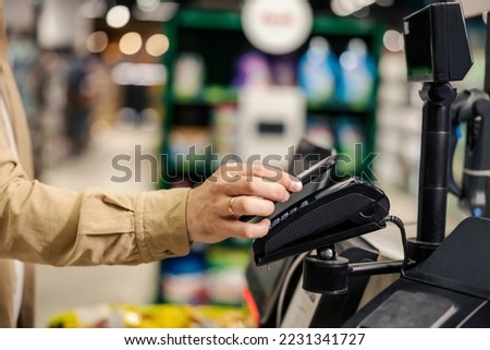Male's hand paying with pone app on self-service checkout at hypermarket.