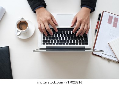 A male's hands are place on laptop with a cup of coffee and document chart on white table in office, Closed up, Mock up, Business.