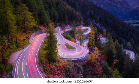 Maloja pass, Switzerland. A road with many curves among the forest. A blur of car lights. Landscape in evening time. 