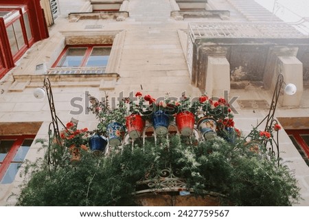Malta. A quaint balcony adorned with a vibrant display of flowers adds a splash of color to the historic architecture. It exudes the charming character of a lively city street.