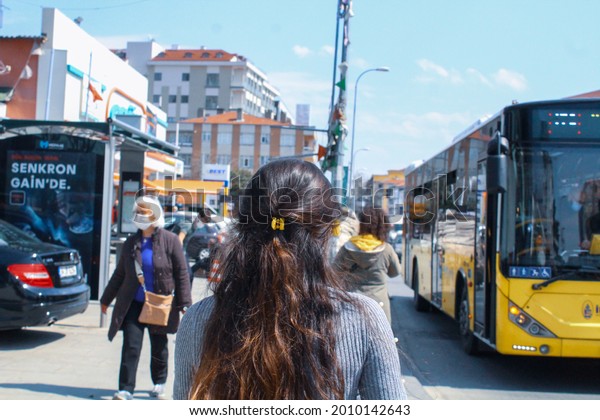 Maltepe, Istanbul, Turkey - 04.15.2021: a young\
brunette woman with mask walking towards the bus station to get on\
a municipality bus in corona virus quarantine days under blue sky\
in summer time