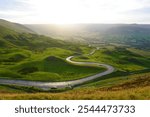 Mam Tor in the Peak District features a winding scenic road through lush green hills and valleys, offering breathtaking views across Derbyshire