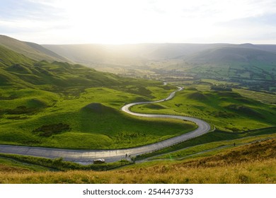 Mam Tor in the Peak District features a winding scenic road through lush green hills and valleys, offering breathtaking views across Derbyshire's iconic countryside. - Powered by Shutterstock