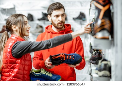 Mam And Woman In Red Sports Clothes Choosing Trail Shoes For Hiking Standing Near The Showacase Of The Modern Sports Shop