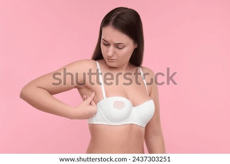 Mammology. Woman in bra doing breast self-examination on pink background