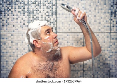 A Man Of 30-40 Years Old In A Foam Stands In The Bathroom, Looking Forward To A Shower, Water Does Not Pour. Water Supply Failure