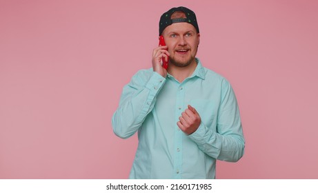 Man 30s In Blue Shirt Having Pleasant Mobile Conversation Using Smartphone With Friends, Telling Good News. Young Adult Blonde Guy Talking On Cell Phone Isolated Alone On Pink Studio Wall Background