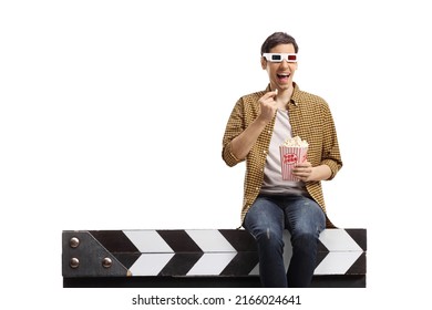 Man With 3d Glasses Sitting On A Movie Clapper Board And Eating Popcorn Isolated On White Background